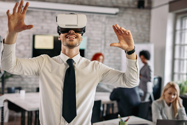 Happy businessman testing virtual reality headset and having fun in the office. There are people in the background.  - Foto, Imagen