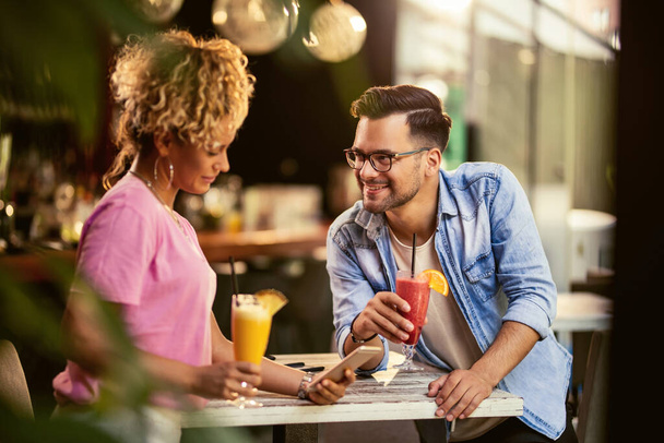 Молода усміхнена пара розслабляє і п'є фруктові коктейлі в кафе. Жінка текстові повідомлення на мобільному телефоні
.  - Фото, зображення