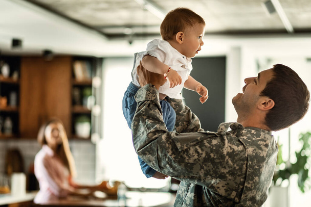 Щасливий солдат армії грає зі своїм маленьким сином і розважається вдома. Мама на задньому плані
.  - Фото, зображення