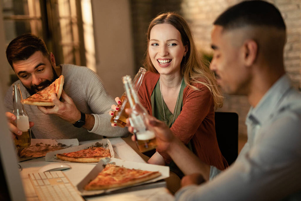 Happy female entrepreneur and her male colleagues eating pizza and drinking beer on a break in the office.  - Photo, Image