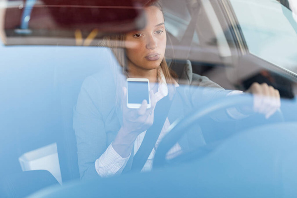Young pensive businesswoman making a phone call while driving a car. The view is through the glass.  - Photo, Image