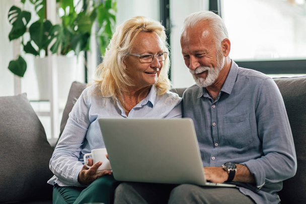 Happy senior couple enjoying while surfing the net together on laptop in the living room.  - Φωτογραφία, εικόνα