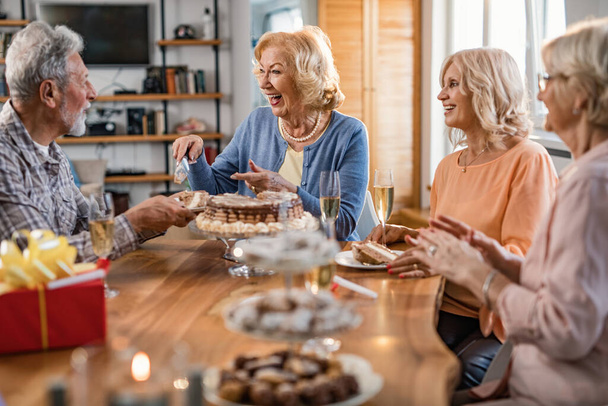Щаслива старша жінка розважається на день народження, подаючи торт і спілкуючись з друзями вдома
.  - Фото, зображення