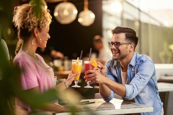 Happy man and his girlfriend toasting with cocktails and having fun in a bar.  - 写真・画像