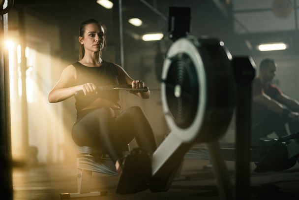 Young athletic woman exercising on rowing machine during cross training in a gym.  - Foto, imagen