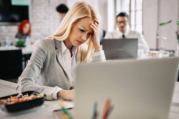 Businesswoman holding her head in pain while being worried about the problems she has at work. There are people in the background.  - Photo, image