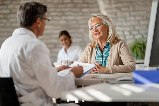 Счастливая зрелая женщина, которая консультируется со своим врачом и говорит о возможностях медицинского страхования в клинике.  - Фото, изображение