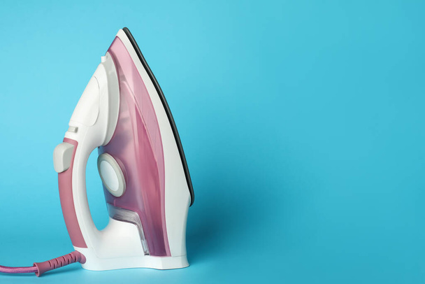 One modern iron on light blue background, space for text. Home appliance - 写真・画像
