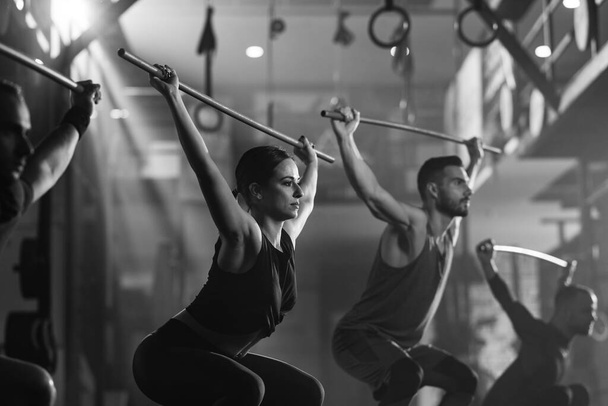 Black and white photo of athletic people exercising with rods on cross training in a gym. - Foto, Imagen