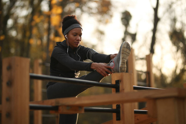 African American female athlete warming up while doing stretching exercises at outdoor gym.  - Foto, imagen
