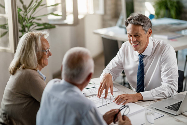Happy insurance agent and senior couple talking while going through paperwork on a meeting in the office. - Photo, Image
