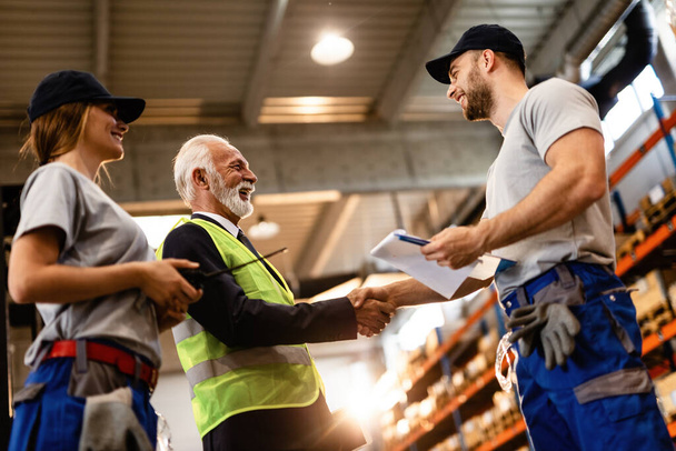 Low angle view of happy workers greeting mature manager in a factory warehouse. Men are shaking hands.  - Foto, immagini