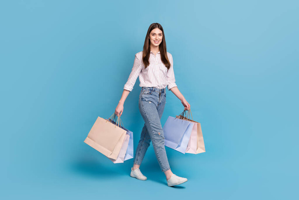Full length body size view of attractive cheerful girl carrying bags going isolated over bright blue color background. - Foto, Imagem