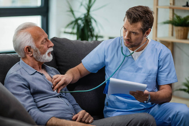 Healthcare worker using stethoscope and listening to heartbeat of his mature patient during a home visit.  - Foto, Bild