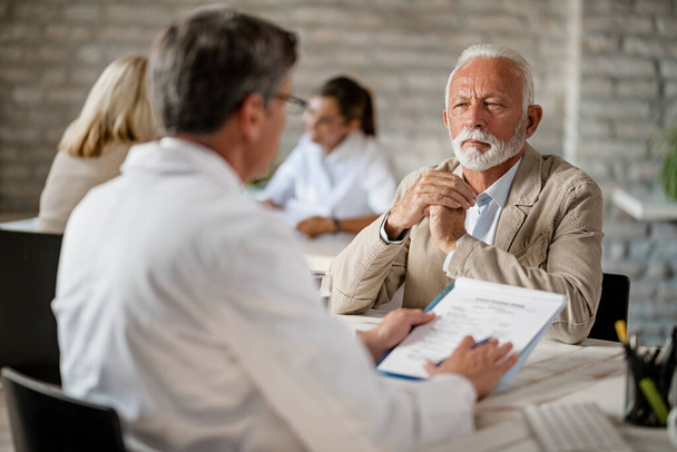 Senior man and healthcare worker communicating about medical insurance documents during a meeting at clinic.  - Foto, Imagem