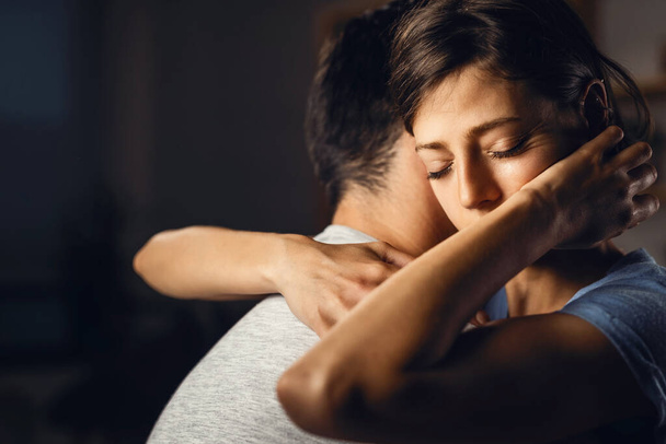 Young distraught woman with eyes closed being embraced by her boyfriend. - Фото, изображение