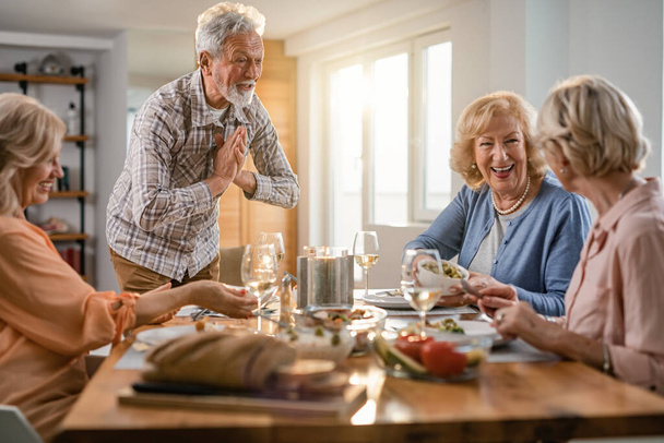 Счастливый старший мужчина наслаждается, разговаривая со своими подругами за обедом дома - Фото, изображение