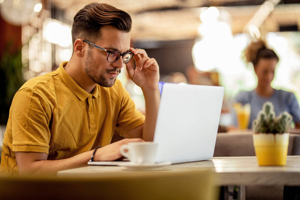 Σοβαρός ελεύθερος επαγγελματίας που εργάζεται σε έναν υπολογιστή και διαβάζει ένα e-mail ενώ κάθεται σε ένα καφέ.  - Φωτογραφία, εικόνα