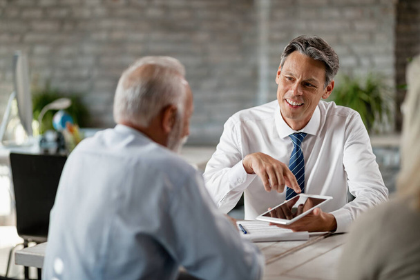 Счастливый банковский менеджер с помощью тачпада во время разговора со старшими клиентами на встрече в офисе.  - Фото, изображение