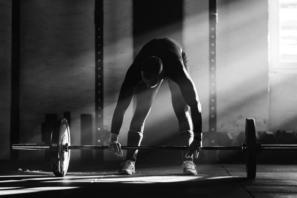 Чорно-біла фотографія спортсмена, який піднімає штангу на перехресній підготовці в клубі охорони здоров'я
.  - Фото, зображення
