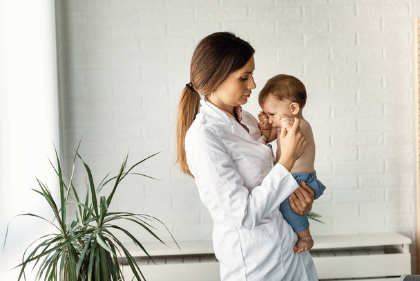 Female doctor consoling a sad small boy against the wall at doctor's office.  - Foto, imagen