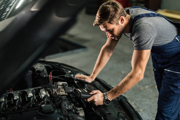 Auto mechanic doing car battery check while using diagnostic tool in a service workshop.  - Fotoğraf, Görsel