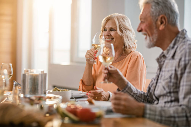 Счастливая пожилая пара наслаждается бокалом вина во время обеда за обеденным столом. В центре внимания - женщина.  - Фото, изображение