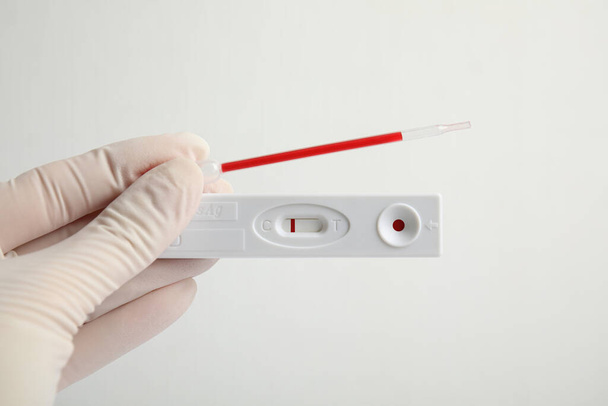 Doctor holding disposable express test for hepatitis and pipette with blood on white background, closeup - 写真・画像