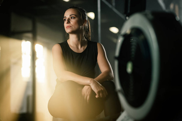 Young athletic woman resting after exercising on rowing machine in a gym. - Fotó, kép