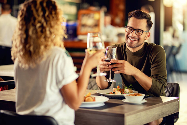 Young happy man communicating with his girlfriend while having a lunch and drinking wine in a restaurant.  - Foto, Bild
