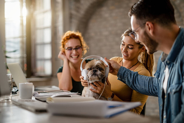 Team of creative business colleagues having fun while giving headphones to a dog in the office. Focus is on dog.  - Foto, Imagen