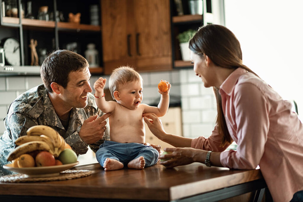 Happy military man and his wife tickling their baby son and having fun at home.  - Foto, imagen