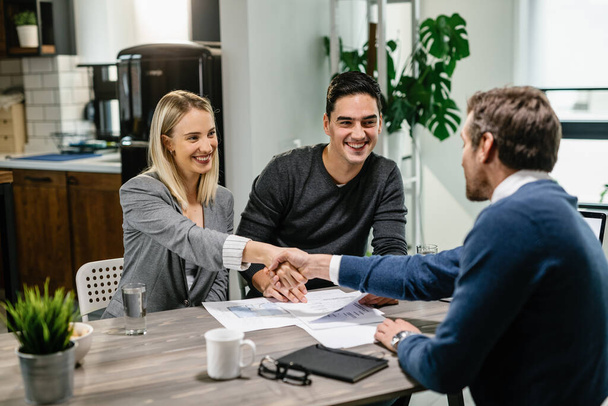 Young happy couple making a deal with financial advisor while having a meeting at their home. Woman is shaking hands with the advisor.  - Photo, Image
