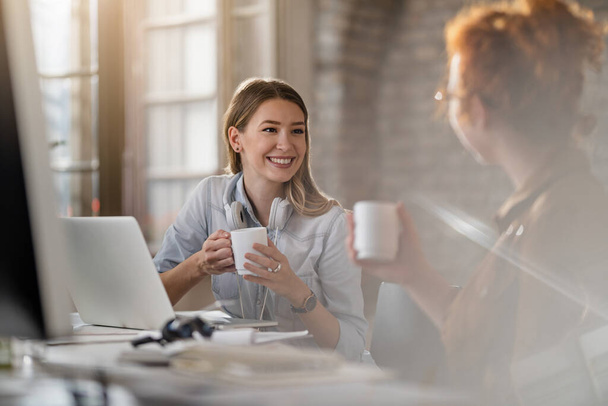 Молода усміхнена бізнес-леді та її колега спілкуються під час кави в офісі
.  - Фото, зображення