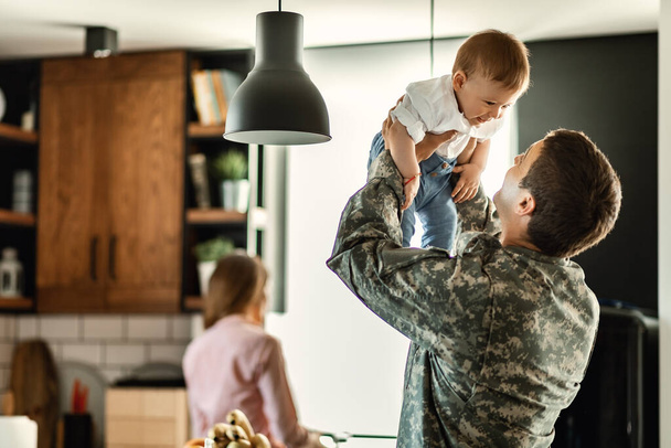 Счастливый мальчик развлекается дома со своим военным отцом. Мама на заднем плане..  - Фото, изображение