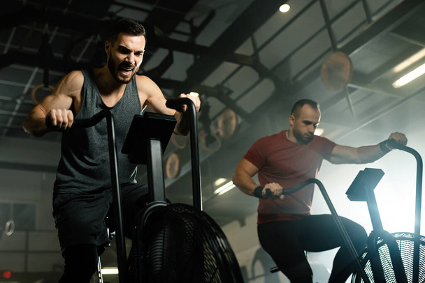 Low angle view of determined male athletes having sports training on exercise bikes in health club.  - Φωτογραφία, εικόνα