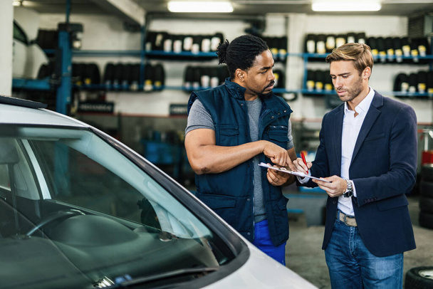 Young black auto mechanic and his manager communicating while going through checklist in a repair shop.  - Foto, immagini