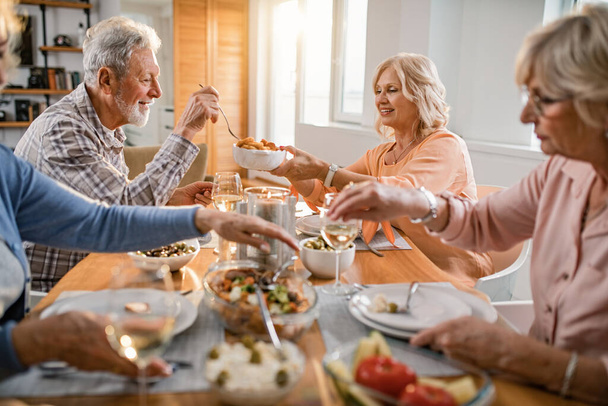Happy senior couple sharing food while having lunch with their friends at home.  - 写真・画像