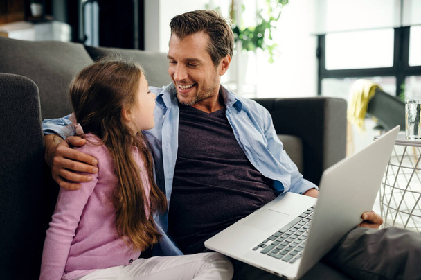 Happy father embracing his daughter and talking to her while surfing the net on a computer at home.  - Foto, immagini