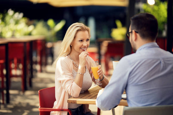 Щаслива жінка розмовляє зі своїм хлопцем під час пиття соку на побаченні в кафе
.  - Фото, зображення