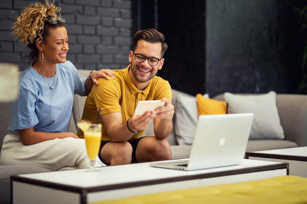 Νεαρό ευτυχισμένο ζευγάρι που διασκεδάζουν ενώ σερφάρετε στο διαδίκτυο στο έξυπνο τηλέφωνο σε ένα καφέ.  - Φωτογραφία, εικόνα