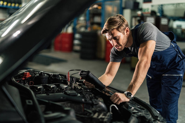 Young auto mechanic doing engine diagnostic while working in repair workshop.  - Foto, Bild