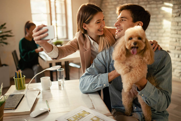 Happy business coworkers with a dog taking selfie while working in the office.  - 写真・画像