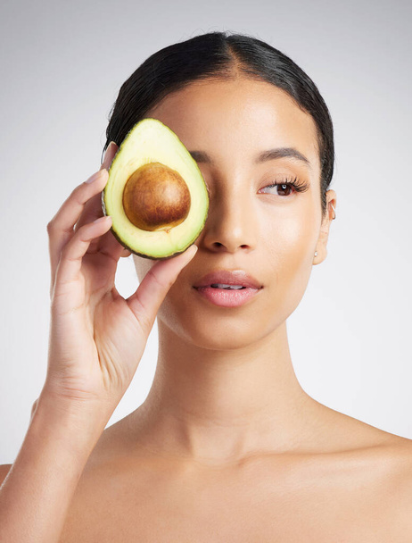A gorgeous mixed race woman holding an avocado. Hispanic model promoting the skin benefits of a healthy diet against a grey copyspace background. - Photo, image