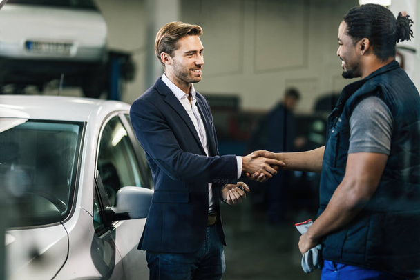 Happy manager and African American car mechanic handshaking in auto repair shop.  - Foto, Imagem