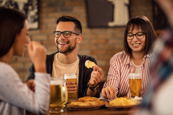 Young happy couple enjoying with friends while drinking beer and having a snack in a tavern.  - Foto, immagini