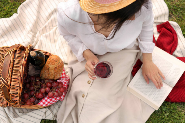 Nő egy pohár bor, könyv és piknik kosár zöld fű, kilátás felett - Fotó, kép