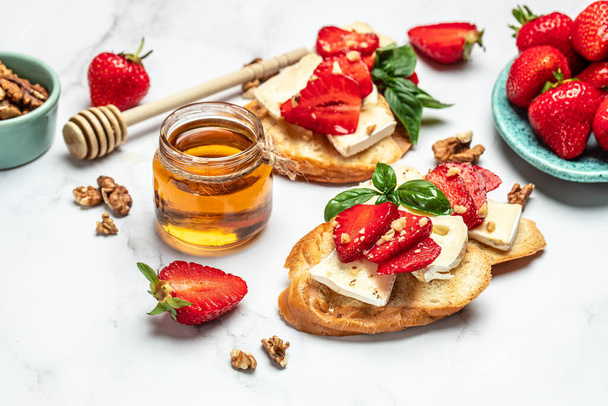 Bruschetta met aardbeien, kaas camembert noten en honing op een lichte achtergrond. Voedselrecept achtergrond. Sluiten.. - Foto, afbeelding