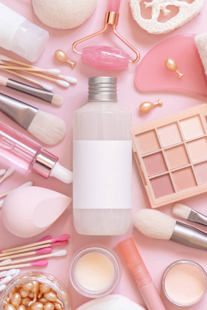 Bottle with blanik label, skin care and decorative cosmetics on pink, top view, mockup. Flat lay with natural beauty products and decorative cosmetics. Everyday woman face care routine  - 写真・画像