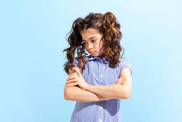 Ofendida. Retrato de niña guapa, niña en edad escolar en vestido de verano aislado sobre fondo azul. Concepto de emociones infantiles, moda, belleza, vuelta a la escuela y anuncio - Foto, Imagen